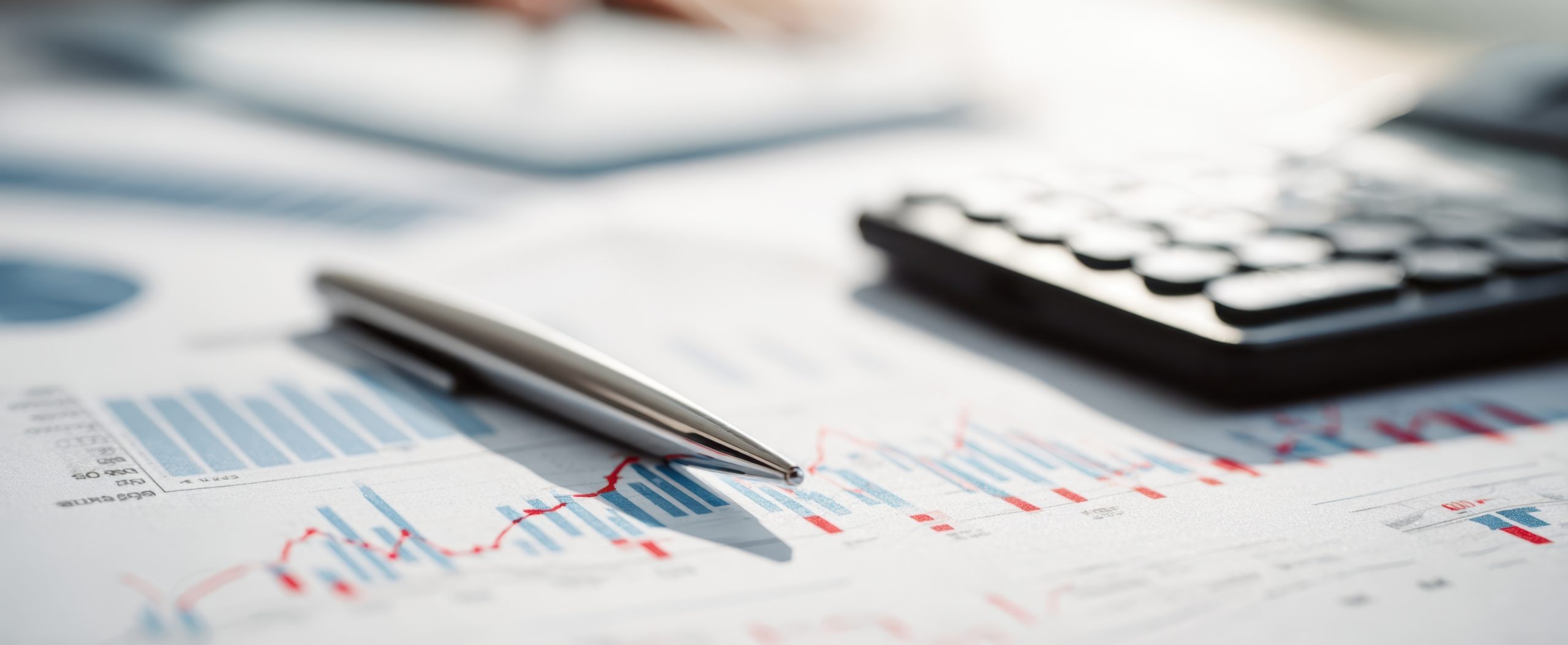 The pen resting on financial documents with a calculator and graphs.